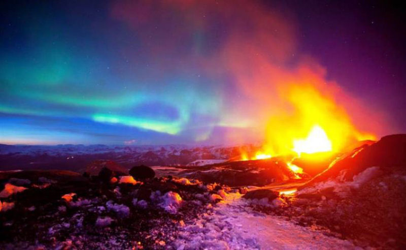 Imagem impressionante de uma erupção de vulcão com a aurora boreal dançando no fundo.