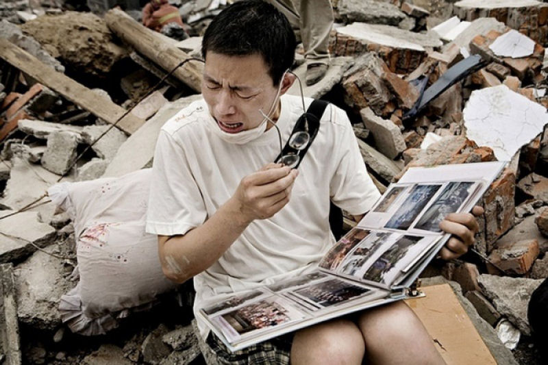 Um homem de Sichuan, China, chora ao ver o lbum familiar perto do que restou de sua casa depois do terremoto.