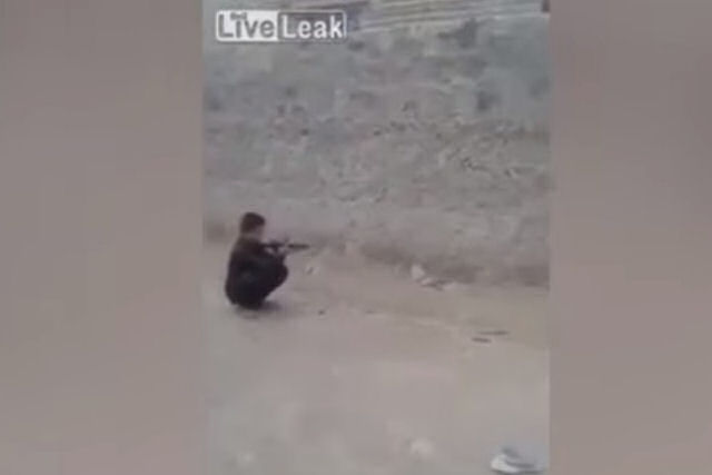 Menino dispara com um rifle contra uma lata sobre a cabeça de seu amigo