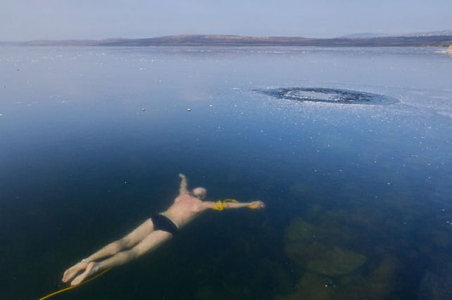 Mergulhador nada sob o gelo de um lago congelado na Repblica Checa