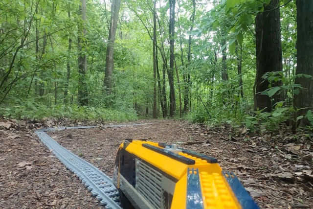 Um pequeno trem LEGO cruza os trilhas através de um bosque canadense em comemoração à primavera