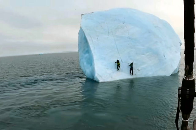 Um iceberg se vira com dois aventureiros em cima no oceano Ártico